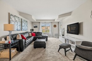 A modern living room with a sectional sofa, a coffee table, a TV mounted on the wall, and a window with a view.
