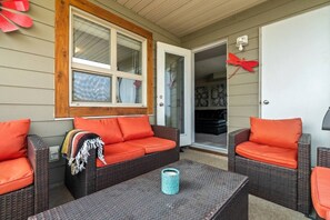 An outdoor seating area with wicker furniture and orange cushions, a glass door leading to a room, and a decorative red butterfly on the wall.