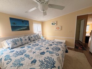 Ein Schlafzimmer mit Bett, Deckenventilator, Gemälde und einer Tür zu einem anderen Raum.