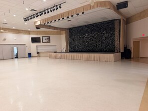 Ein geräumiger Saal mit Bühne, Deckenleuchten und einer Wand mit vertikalen Linien.