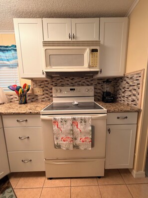 A kitchen with white cabinets, a microwave, a stove, and a blender on the countertop. - Resort style living in North Fort Myers! (North Fort Myers)