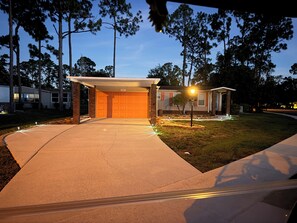Eine Garage mit Wohnhof und überdachter Zufahrt, eine Auffahrt zum Haus sowie ein gepflegter Rasen.