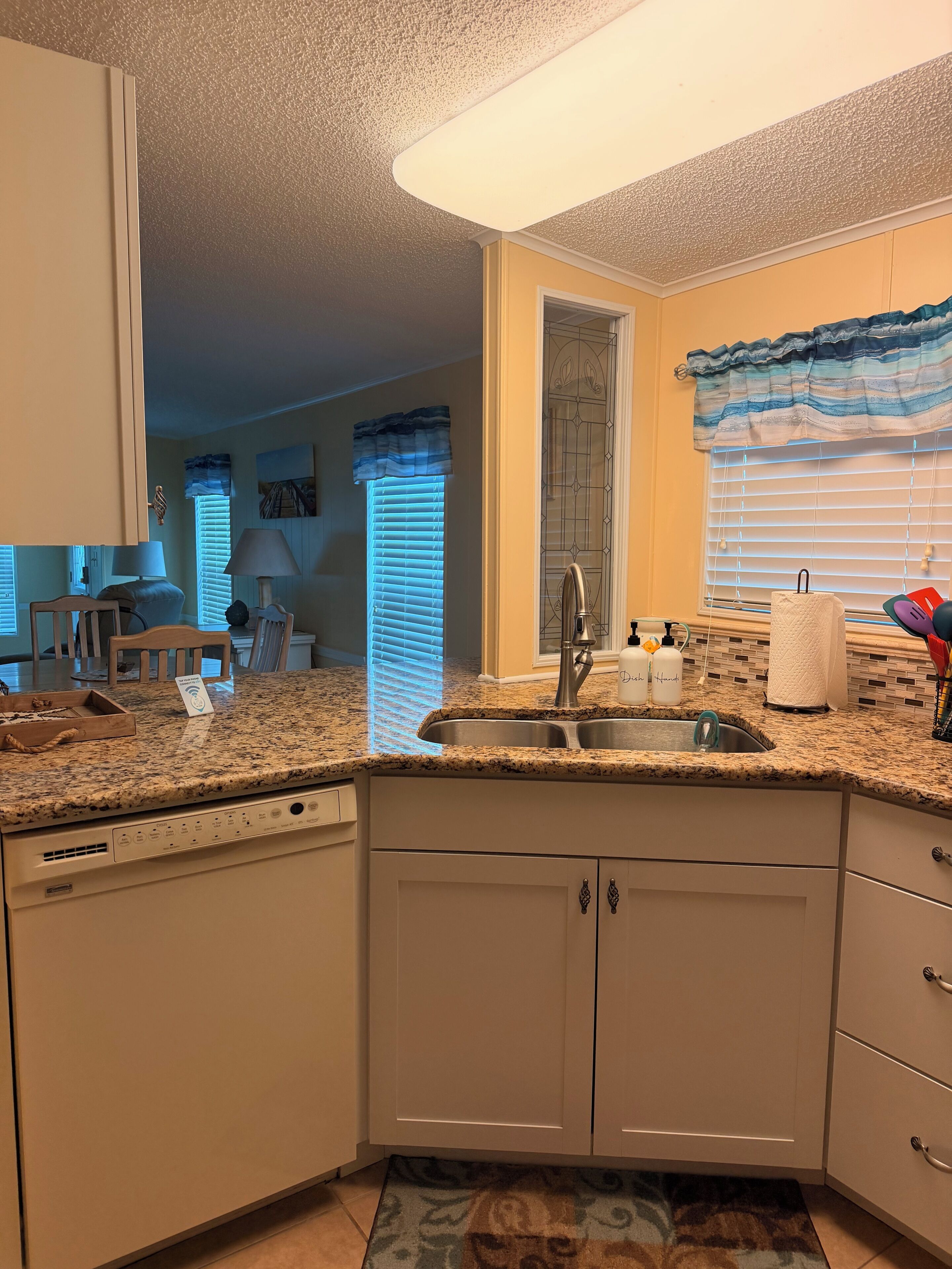 A compact kitchen with a built-in dishwasher, a double sink, and a window with blinds.