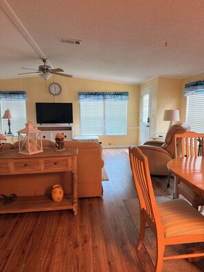 Ein Wohnzimmer mit Deckenventilator, Flachbildfernseher, Esstisch mit Stühlen und einer Couch.