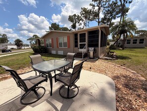 An outdoor patio with a glass table and chairs, a barbecue grill, and a house with a screened porch in the background. - Resort style living in North Fort Myers! (North Fort Myers)
