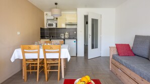 A compact living space with a dining area, kitchenette, and a sofa with a red pillow. - Situé face à la mer | Piscine couverte | Parking (Plougasnou)