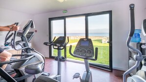 A gym with stationary bikes and a treadmill, large windows with a view of the sea, and a water dispenser. - Situé face à la mer | Piscine couverte | Parking (Plougasnou)