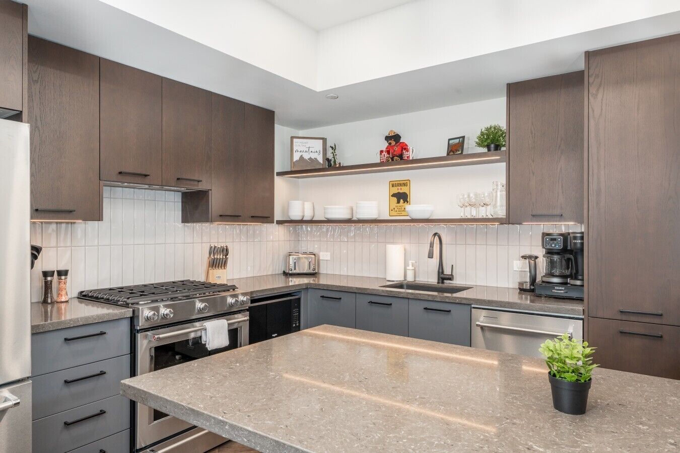 A modern kitchen with dark wood cabinets, a granite countertop, a built-in oven, a stove, a coffee maker, and a small plant.