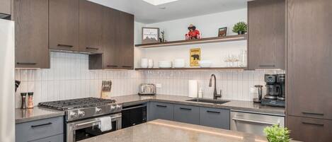 A modern kitchen with dark wood cabinets, a granite countertop, a built-in oven, a stove, a coffee maker, and a small plant.