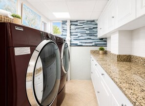 Une buanderie moderne équipée de deux lave-linge à chargement frontal, d’un pare-feu en carrelage et d’un plan de travail en granit.