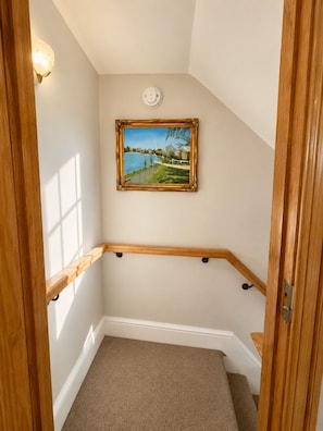Un rincón de una habitación con una escalera de madera, un cuadro en la pared y una lámpara.