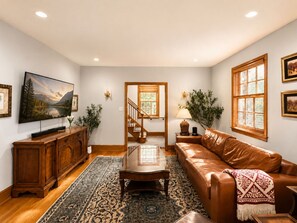 Un salon comprenant un meuble en bois, un canapé en cuir marron, une table basse, un téléviseur posé sur un meuble et un escalier menant à une autre pièce.