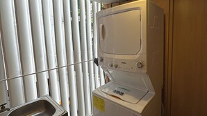 Ein kleiner Waschraum mit Waschmaschine, Spüle und einem Fenster mit Jalousien.