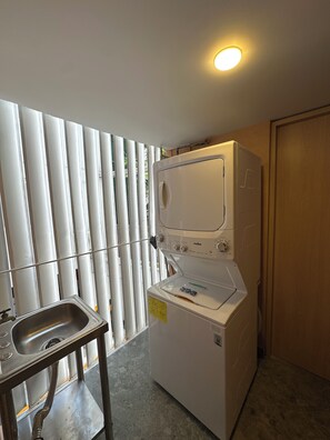 Ein kleiner Waschraum mit Waschmaschine, Spüle und einem Fenster mit Jalousien.