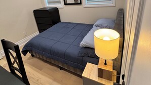 Un dormitorio con cama, mesita de noche, lámpara, silla y un espejo en la pared.