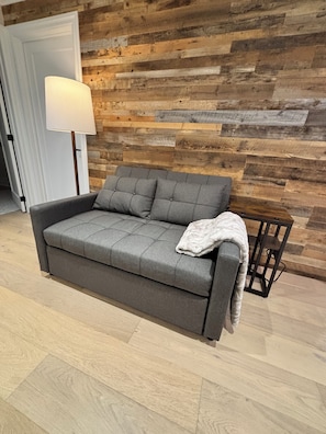 Ein graues Sofa mit weißer Decke, vor einer Holzwand, neben dem ein moderner Lampen steht.