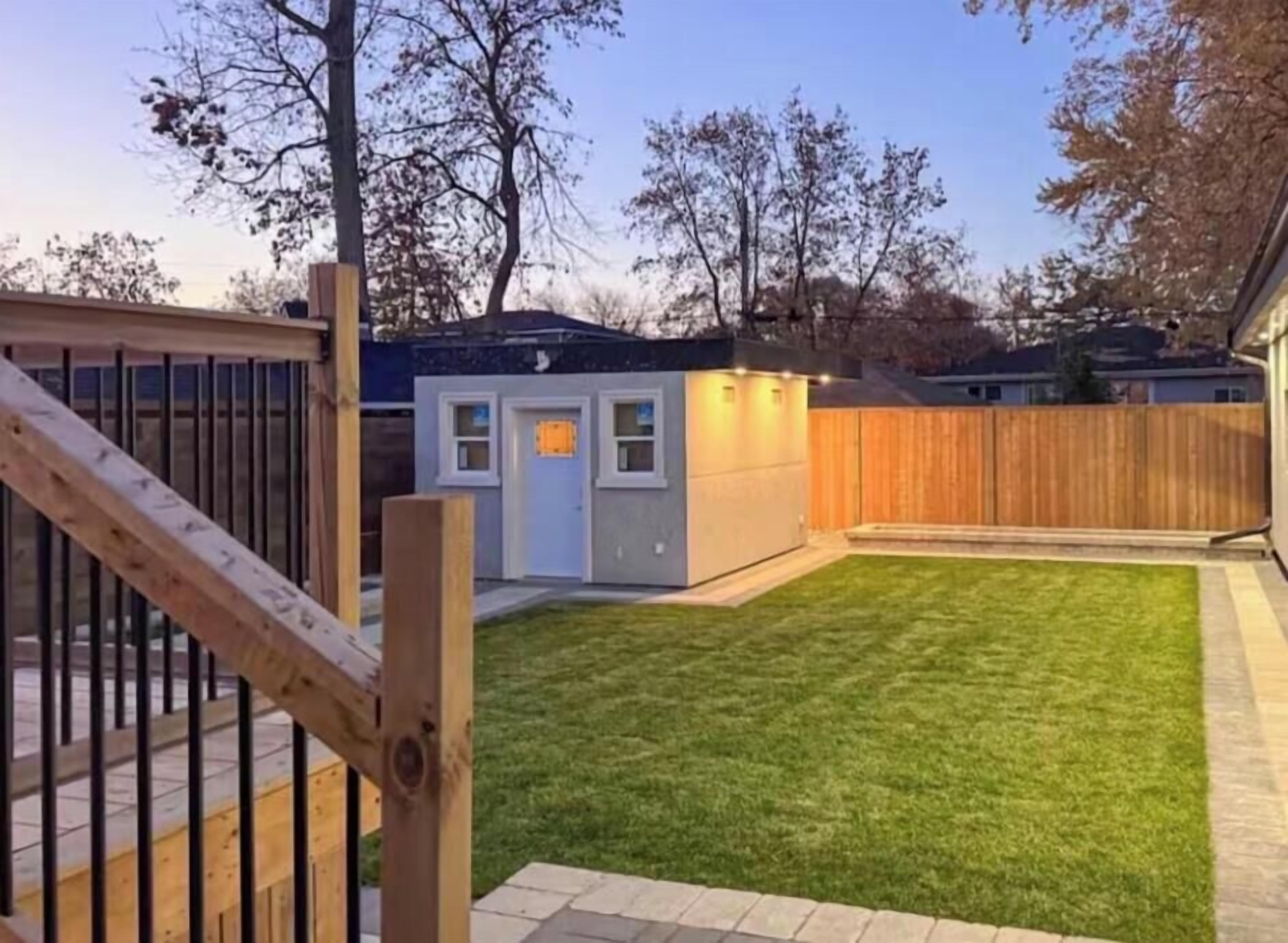 Een achtertuin met een houten terras, een kleine schuur en een verzorgd gazon.
