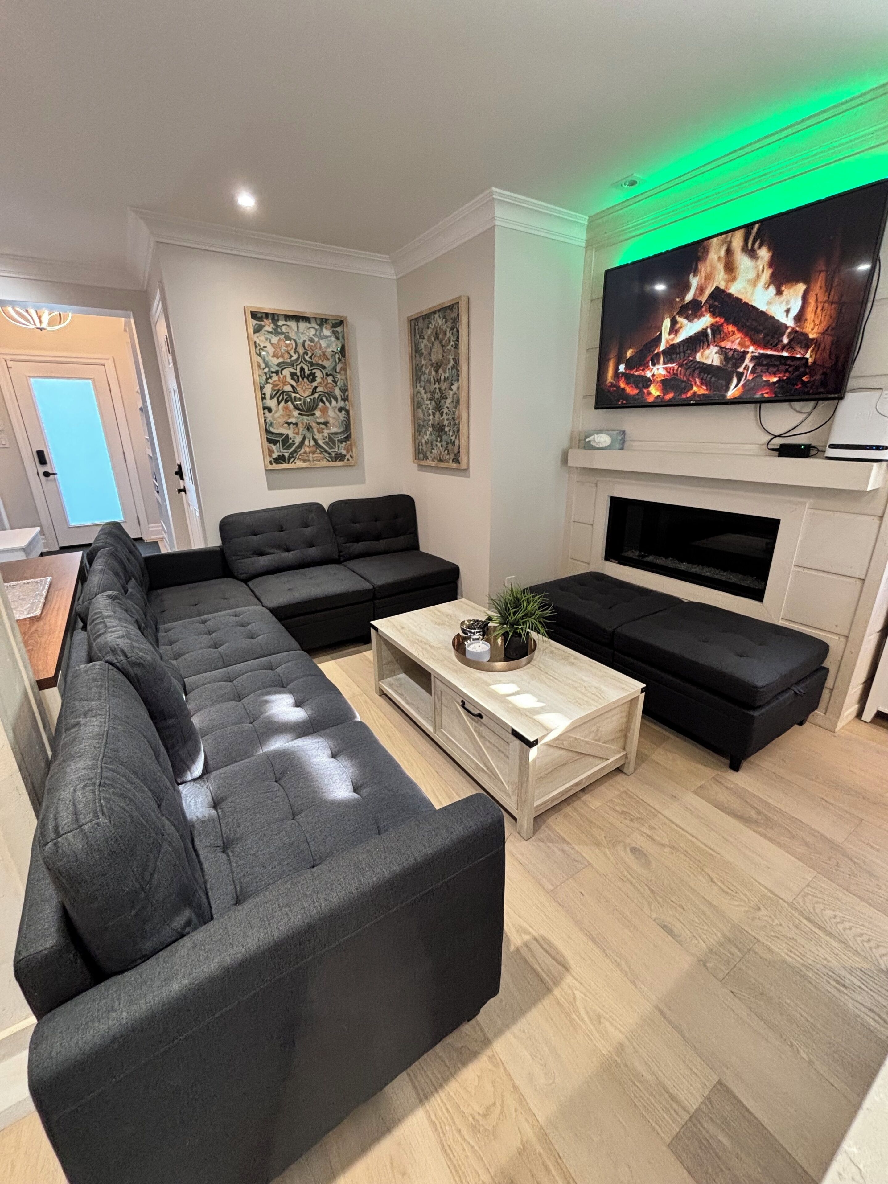 Un salon moderne avec un canapé d’angle, une table basse et un téléviseur à écran plat fixé au-dessus d’une cheminée.