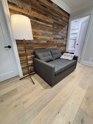 A room with a grey sofa, a floor lamp, and a wooden wall. - 3 bedroom 2 bath I 1 min walk to beach (Georgina)