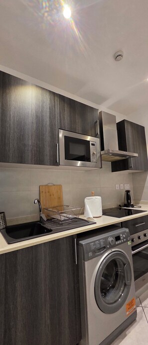 Une cuisine moderne équipée d’un four à micro-ondes encastré, d’une cuisinière, d’un évier et d’un lave-linge.
