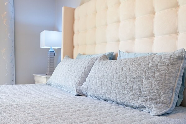 A bed with a quilted headboard, a bedside table with a lamp, and two pillows.