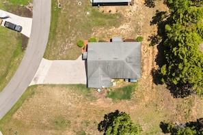 An aerial view of a house with a sloped roof, a driveway, and a small yard with sparse vegetation.