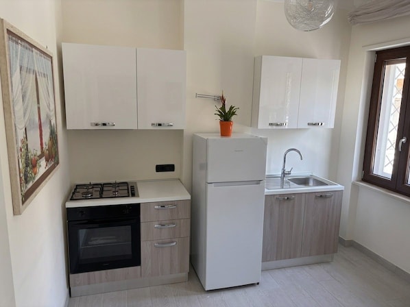 Eine kleine Küche mit weißen Schränken, einem Gasherd, einem Backofen, einem Kühlschrank und einem Spülbecken.