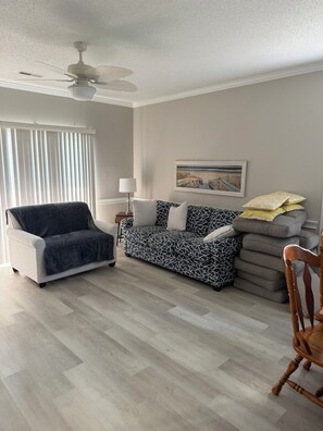 Ein Wohnzimmer mit einer Couch, einem Sessel, einer Lampe und einem Deckenventilator.