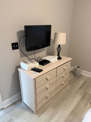 A room with a television mounted on the wall, a lamp on a dresser, and a remote control on the dresser. - Myrtlewood Golf Getaway - Renovated 2BR Condo Near Beach (Myrtle Beach)