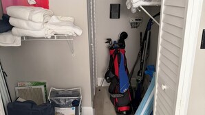 Une petite pièce comprenant un lit, une étagère avec des serviettes pliées, un radiateur, une valise et un tapis bleu.