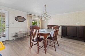 A dining area with a wooden table and chairs, a chandelier, and a view through a window. - Trinity Walk 4 (Steubenville)