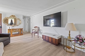 A modern living room with a flat-screen TV, a decorative mirror, a wooden cabinet, and a side table with a lamp.