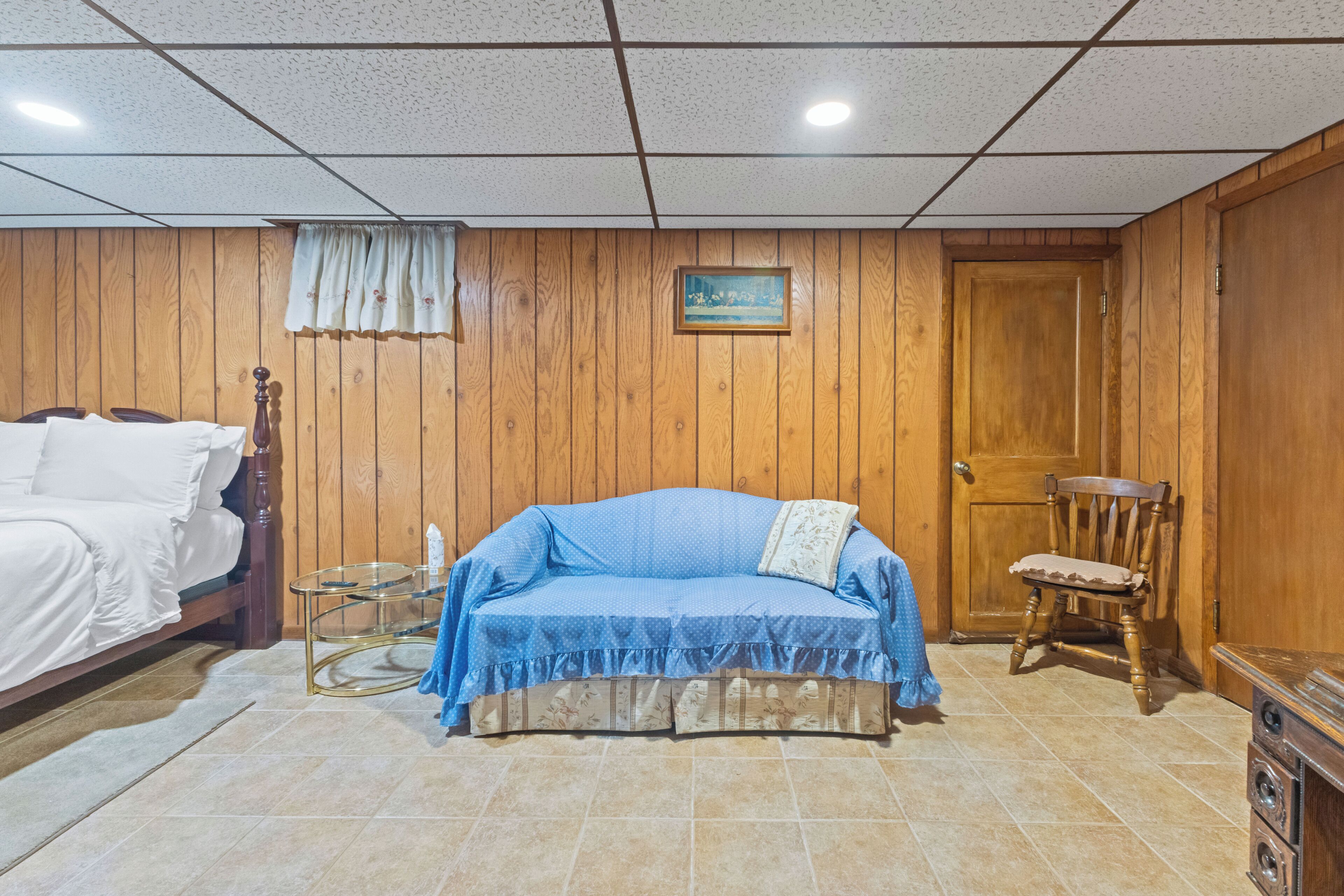 Una habitación con una cama, un sofá, una silla, una mesita y una puerta de madera.