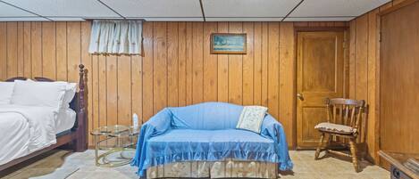 Una habitación con una cama, un sofá, una silla, una mesita y una puerta de madera.