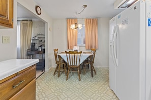 A compact kitchen with a dining table, chairs, a refrigerator, and a coffee machine.