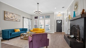 A spacious living room with a blue sofa, a yellow armchair, and a purple chair. There is a fireplace with decorative items and a large window with blinds. - Relaxing Retreat Near Lake Lavon (Wylie)