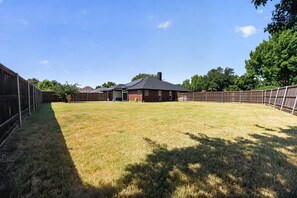 A backyard with a fenced area, a brick house, and a clear sky. - Relaxing Retreat Near Lake Lavon (Wylie)