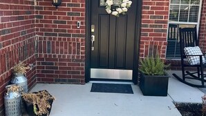 A brick house with a black front door, a wreath, a potted plant, a rocking chair, and a metal lantern. - Relaxing Retreat Near Lake Lavon (Wylie)