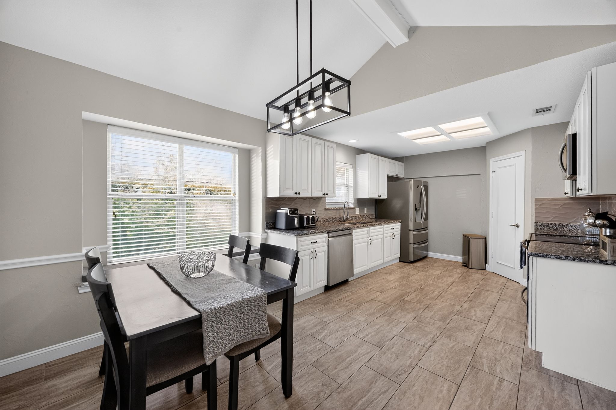 A modern kitchen with white cabinetry, a stainless steel refrigerator, and a dining area with a table and chairs.