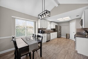 A modern kitchen with white cabinetry, a stainless steel refrigerator, and a dining area with a table and chairs. - Relaxing Retreat Near Lake Lavon (Wylie)