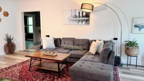 Ein modernes Wohnzimmer mit einem Ecksofa, einem Couchtisch und einem gemusterten Teppich.