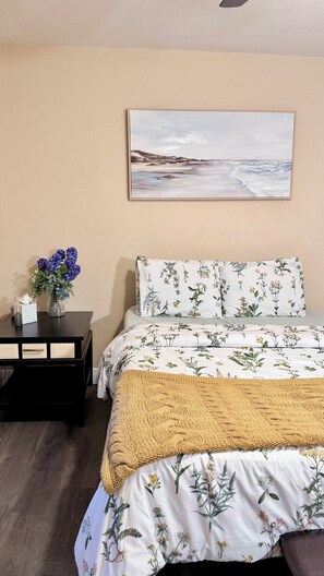 Ein Schlafzimmer mit einem Bett, einem Nachttisch, einem Gemälde und einer Vase mit Blumen.