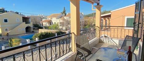 A balcony with a glass table, chairs, and a bottle of wine.