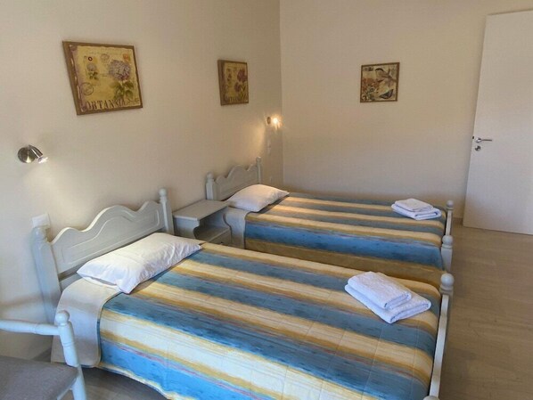 Une chambre avec deux lits, chacun recouvert d’une couvre-lit à rayures et agrémenté d’oreillers blancs, une table de chevet avec une lampe et une porte.