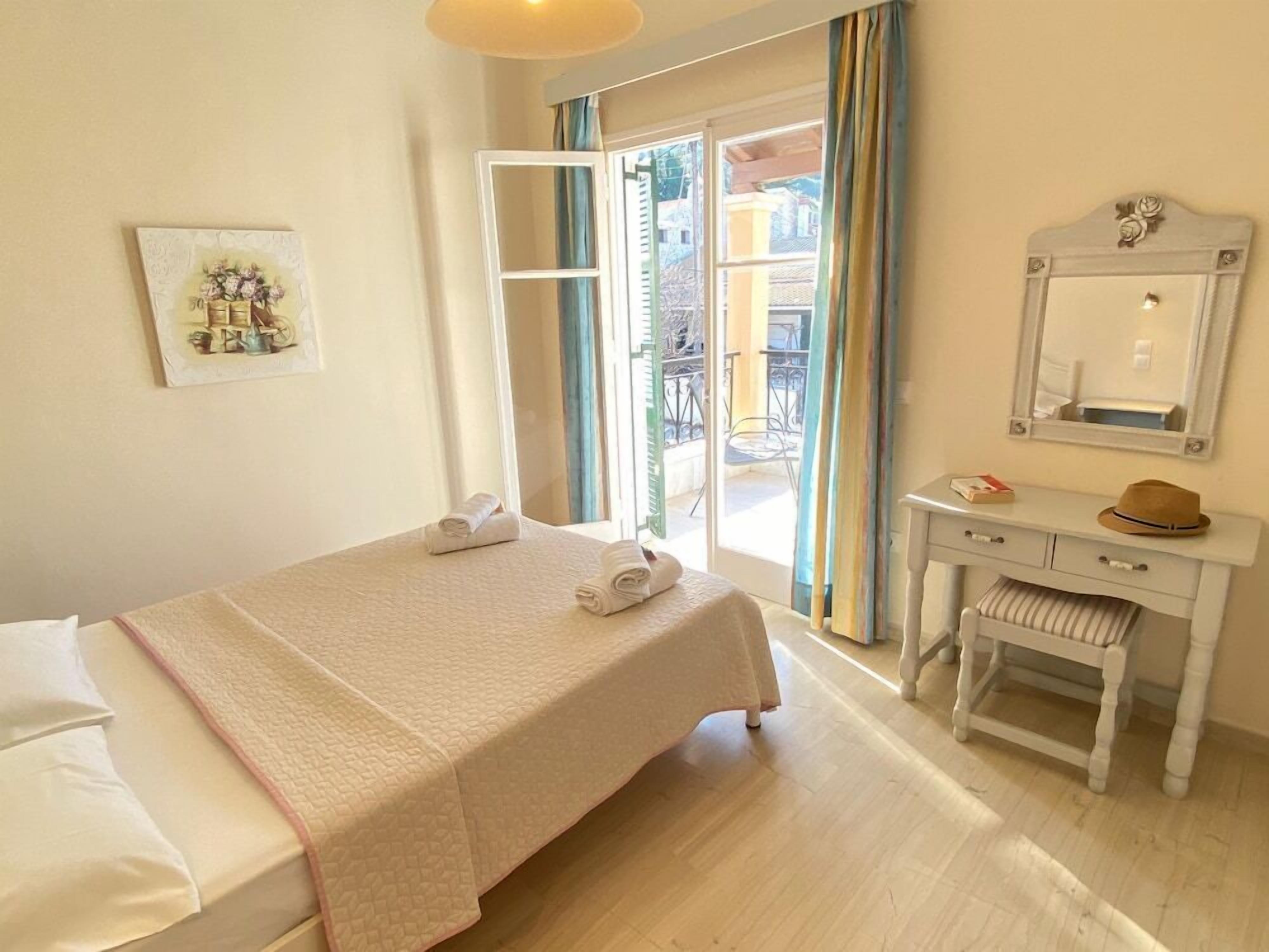 A hotel room with a bed, a desk, a chair, a mirror, and a window with curtains.