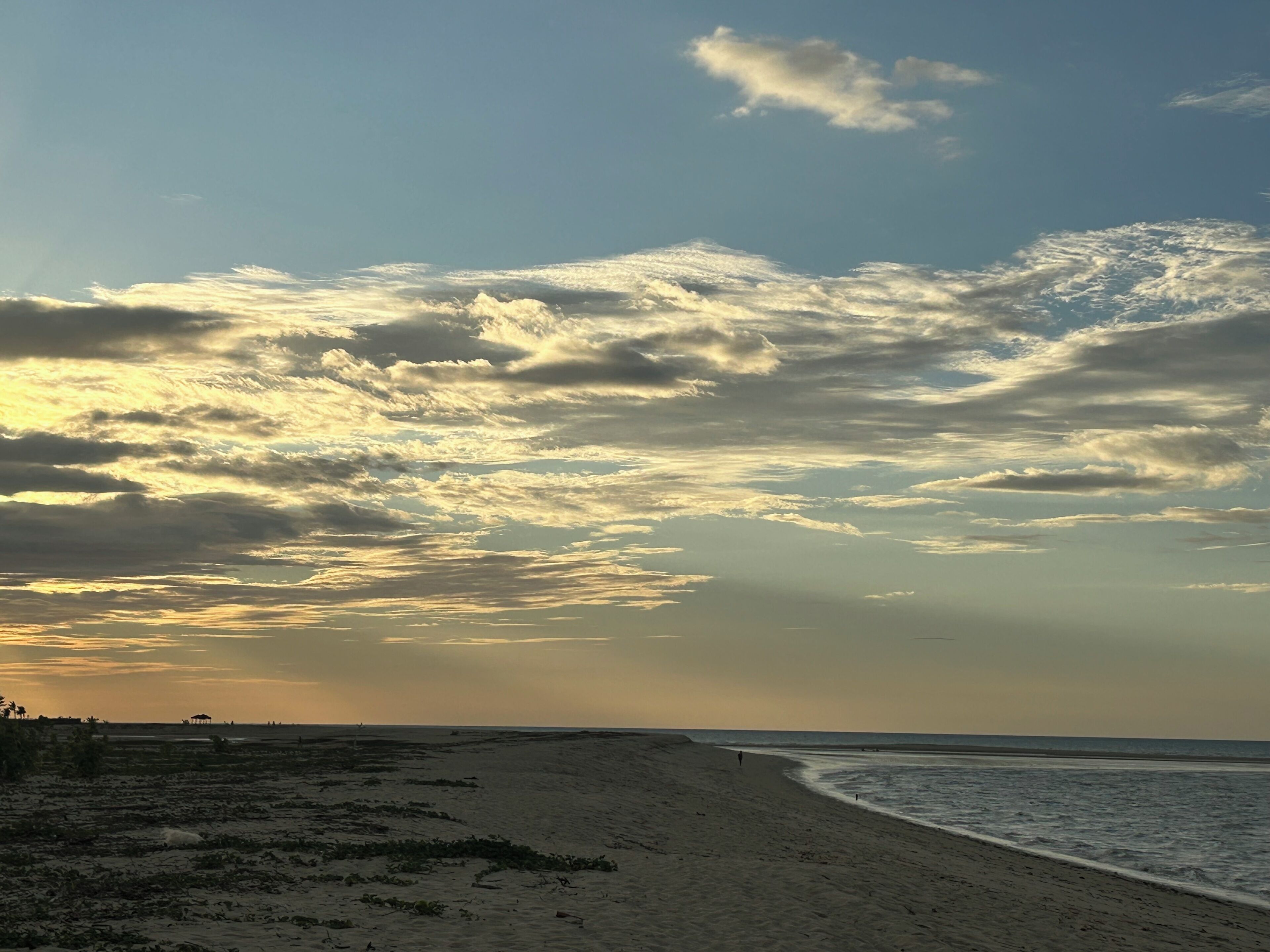 Una playa con una extensa orilla arenosa y un cielo despejado con algunas nubes.