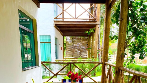 Une terrasse en bois avec une table ronde et des chaises à rayures, entourée d’une clôture en bambou.