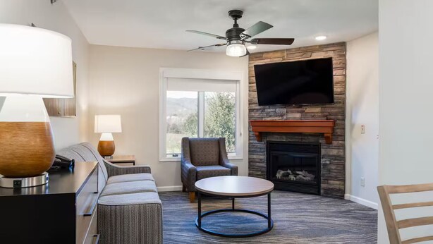 A living room with a fireplace, a television mounted above it, a ceiling fan, and a view of the outdoors through a window. - Escape to Massanutten: Your Ultimate July 4th Getaway! #1 (Massanutten)