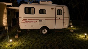 Un camping-car Scamp blanc est garé sur une pelouse, la nuit.