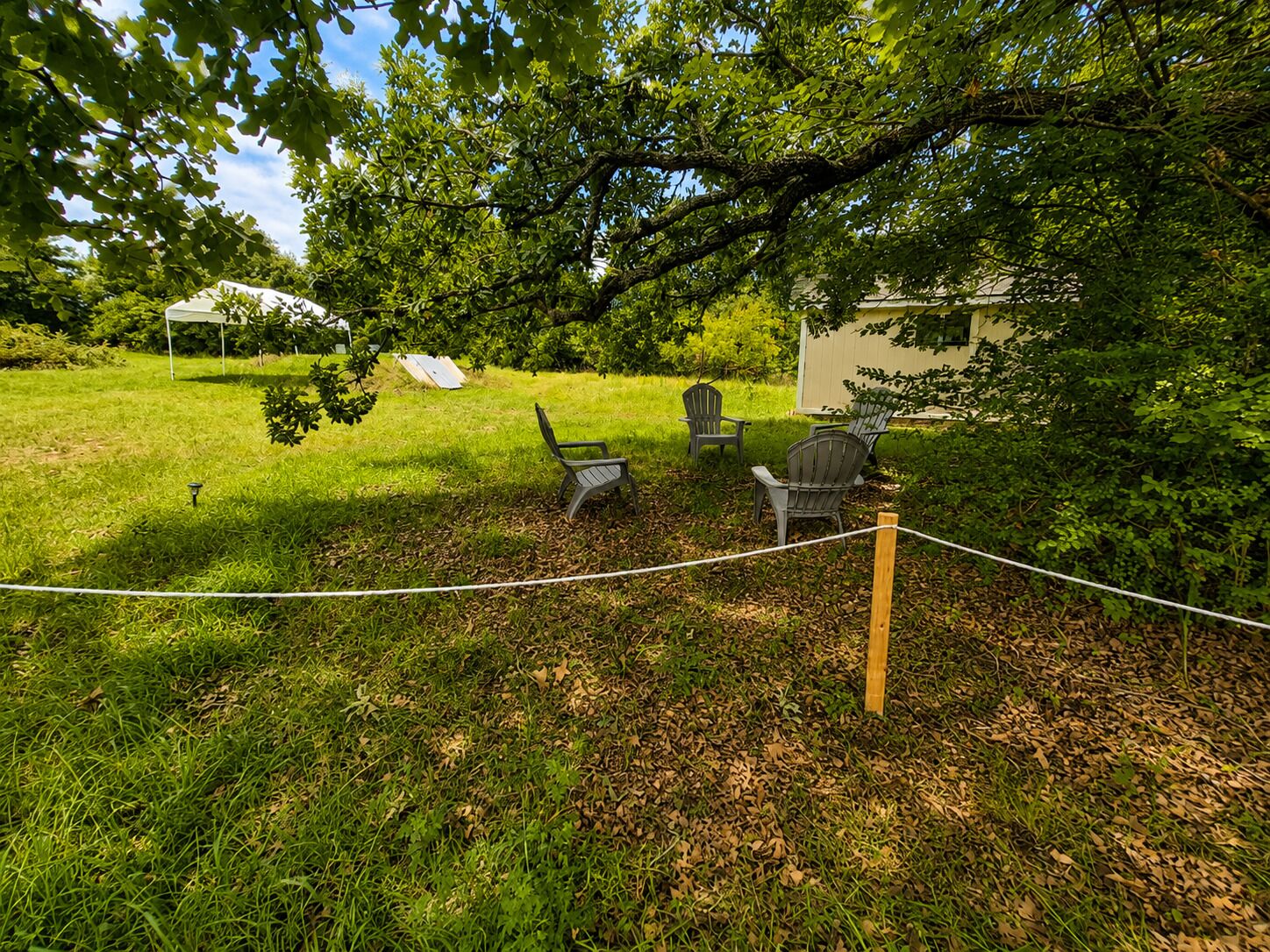 Un espace extérieur verdoyant, d élimité par une barrière en corde, avec trois fauteuils Adirondack et un petit abri de jardin.
